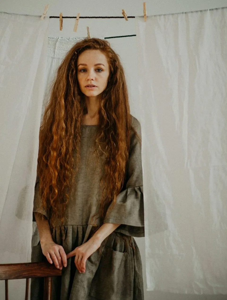 Elegant woman in a rustic dress standing with linens background, exuding a vintage charm.